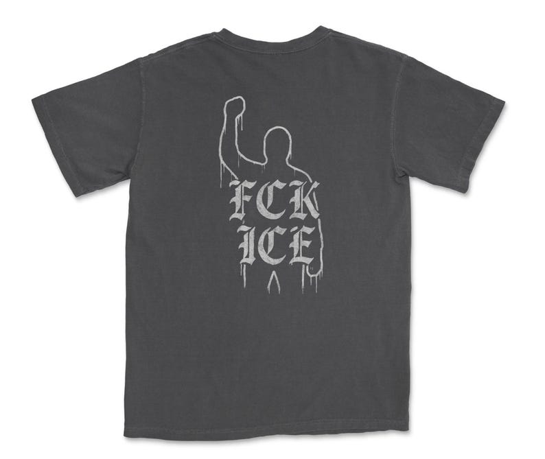 Puede incluir: Camiseta gris oscuro con un gr&aacute;fico blanco en la espalda. El gr&aacute;fico presenta una silueta de pu&ntilde;o en alto con el texto "FCK ICE" en una fuente g&oacute;tica. La camiseta tiene mangas cortas y cuello redondo.