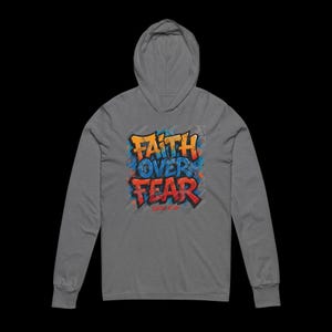Peut inclure: Un sweat &agrave; capuche gris &agrave; manches longues. Le devant affiche les mots "FAITH OVER FEAR" dans un style graffiti. Le texte est en orange et rouge avec des accents bleus. Le sweat &agrave; capuche a une capuche et une coupe d&eacute;contract&eacute;e.