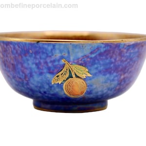 May include: A small, round blue bowl with a gold rim and a gold and orange fruit design. The bowl has a textured surface and a dark blue base. The website address "www.coscombefineporcelain.com" is visible at the top.