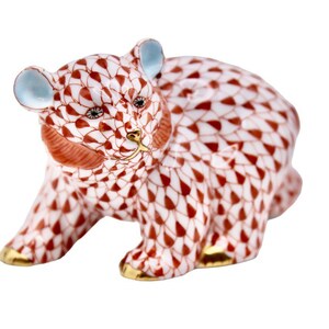 May include: A porcelain bear figurine with a white and red pattern. The bear has blue ears, gold accents on its paws and snout, and small black eyes. The figurine is a decorative item.