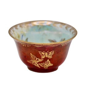 May include: A small, antique-style bowl with a reddish-brown exterior and a light blue interior. The bowl is decorated with gold butterfly designs and gold trim around the rim. The bowl has a rounded shape and sits on a white background.