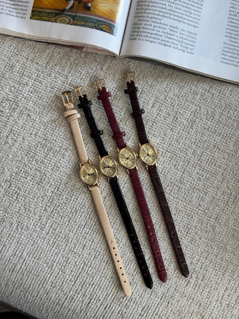 K&ouml;nnte beinhalten: Vier Damenuhren mit goldfarbenen Geh&auml;usen und Lederarmb&auml;ndern in Beige, Schwarz, Burgunderrot und Braun. Die Uhren haben ein ovales Zifferblatt mit r&ouml;mischen Ziffern und eine Schnalle.