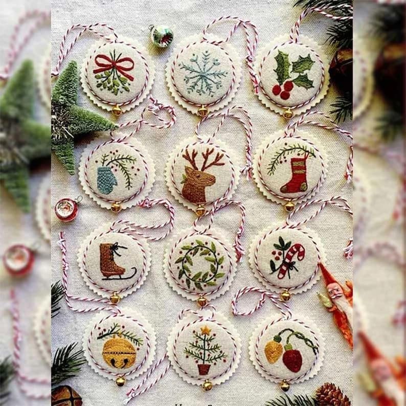 May include: A collection of embroidered Christmas ornaments with various festive designs, including a snowflake, holly, and a reindeer. Each ornament is round, with a scalloped edge and a red and white string for hanging. The ornaments are embellished with small gold bells.
