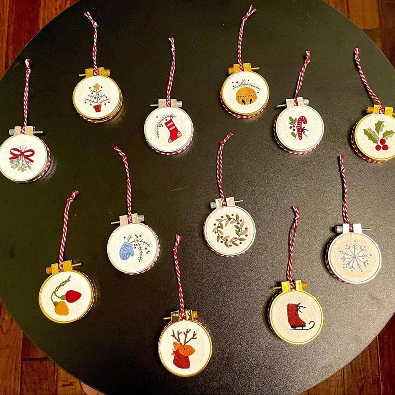 May include: A collection of embroidered Christmas ornaments. Each ornament is round, featuring festive designs like a Christmas tree, snowflake, and holly. They have a red and white striped hanging cord and are set against a dark background.
