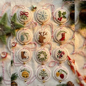 May include: A collection of embroidered Christmas ornaments with various festive designs, including a snowflake, holly, and a reindeer. Each ornament is round, with a scalloped edge and a red and white string for hanging. Small gold bells are attached.