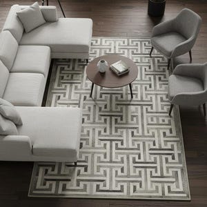 May include: An overhead view of a modern living room with a light gray sectional sofa, two gray armchairs, and a round brown coffee table. A geometric patterned rug in shades of gray and white covers the floor. A floor lamp and a potted plant are also visible.