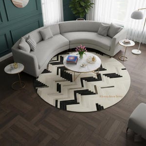 Puede incluir: Un salón moderno con un sofá gris curvo, una alfombra redonda estampada y mesas auxiliares. Una mesa de centro con tapa de mármol y patas doradas está en el centro. La habitación tiene suelo de madera oscura y una lámpara de pie. El texto "Elyssia decor home" es visible.