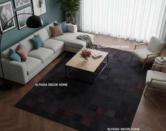 May include: An interior shot of a living room with a large, dark, patchwork rug. A light-colored sectional sofa with throw pillows sits against a teal wall. A wooden coffee table with a black metal frame and a bouquet of flowers is in the center.