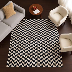 May include: Overhead view of a black and cream-colored chevron patterned rug. The rug is centered in a room with a gray sofa, two cream-colored armchairs, and a small round wooden table. A tan pillow rests on the sofa.