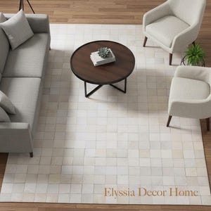 May include: A living room scene with a light grey sofa, two armchairs, and a round coffee table. A cream-coloured rug with a square pattern sits on a wooden floor. The text "Elyssia Decor Home" is visible on the rug. The rug is approximately 200 cm x 300 cm.