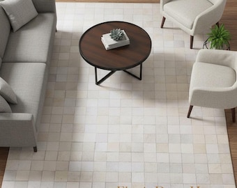 May include: An overhead shot of a living room setup featuring a light gray sofa, two armchairs, and a round coffee table. A cream-colored rug with a square pattern is centered on the wooden floor. The text "Elyssia Decor Home" is visible on the rug.
