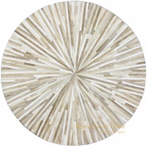 May include: A round rug with a sunburst design. The rug is made of rectangular pieces of cowhide in shades of beige, cream, and light brown. The design radiates from the center, creating a starburst pattern. The rug is a decorative floor covering.