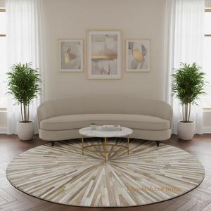 May include: A beige curved sofa, a round marble-topped coffee table with a gold base, and a large circular rug with a sunburst pattern. Three framed abstract art pieces hang above the sofa. Two potted plants flank the sofa.