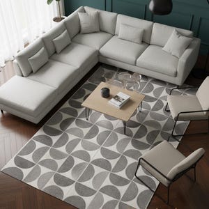 Könnte beinhalten: Moderne Wohnzimmereinrichtung mit einem hellgrauen Ecksofa und Kissen. Ein geometrischer Teppich in Grau- und Weißtönen liegt unter einem Holztisch. Zwei Stühle und eine Stehlampe vervollständigen den Raum. Modernes Ambiente.