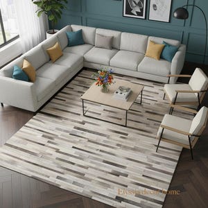 Puede incluir: Un salón moderno con un sofá seccional gris claro, cojines coloridos, una mesa de centro de madera y dos sillones. Una gran alfombra con un patrón de rayas y un suelo de madera completan el espacio. Obras de arte cuelgan en la pared turquesa.