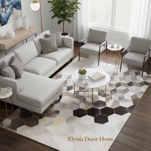 Könnte beinhalten: Ein modernes Wohnzimmer-Setup mit einem hellgrauen Ecksofa, zwei Sesseln und einem geometrischen Teppich. Der Teppich hat ein sechseckiges Muster in Weiß-, Grau- und Brauntönen. Ein Marmor-Couchtisch und eine Stehlampe vervollständigen die Einrichtung.