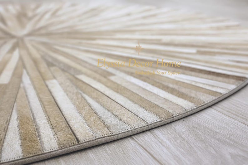 May include: A beige and cream-colored round rug with a radial pattern. The rug is made of rectangular pieces of material sewn together, creating a sunburst design. The rug has a stitched border and is placed on a light-colored wooden floor.