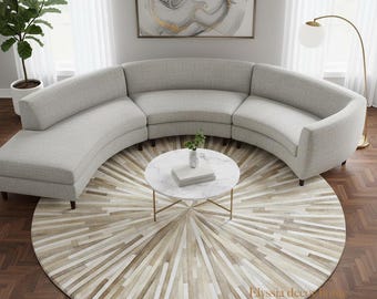 May include: A light gray, curved sectional sofa with a matching round coffee table and a patterned rug. The rug has a sunburst design in shades of beige and white. A floor lamp with a white globe shade and a potted plant are also visible.