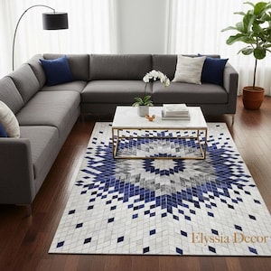 Könnte beinhalten: Ein modernes Wohnzimmer mit einem großen grauen Ecksofa und blauen Kissen. Ein weißer Marmor-Couchtisch mit goldenem Rahmen steht auf einem gemusterten Teppich mit blauen und weißen geometrischen Designs. Eine Topfpflanze und eine Stehlampe vervollständigen die Einrichtung.