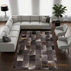Könnte beinhalten: Ein rechteckiger Teppich mit einem Patchwork-Design aus quadratischen Fliesen in verschiedenen Grau-, Braun- und Cremetönen. Der Teppich liegt in einem Raum mit einem großen hellgrauen Ecksofa, zwei hellgrauen Sesseln und einer Stehlampe.