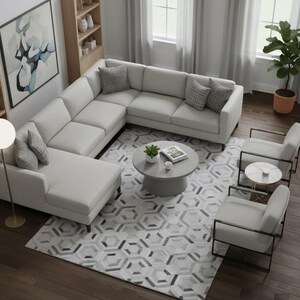 Könnte beinhalten: Draufsicht auf ein modernes Wohnzimmer mit einem hellgrauen Ecksofa, zwei Sesseln und einem runden Couchtisch. Ein gemusterter Teppich und ein Bücherregal aus Holz sorgen für Textur. Ein abstraktes Gemälde hängt an der Wand.