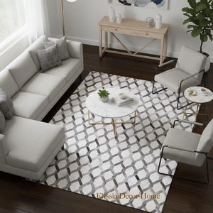 May include: An interior shot of a living room with a light gray sectional sofa, two armchairs, and a round coffee table. A geometric patterned rug in shades of gray and white covers the floor. A wooden console table and a floor lamp are also visible.
