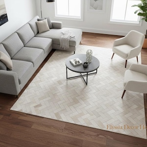 May include: A contemporary living room featuring a grey corner sofa, two cream armchairs, and a black coffee table. A large, light-coloured rug with a herringbone pattern is on a dark wood floor.