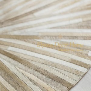 May include: A beige and white cowhide rug with a radial striped pattern. The rug features alternating stripes of light beige, tan, and white, creating a textured surface. The rug is designed for home decor.