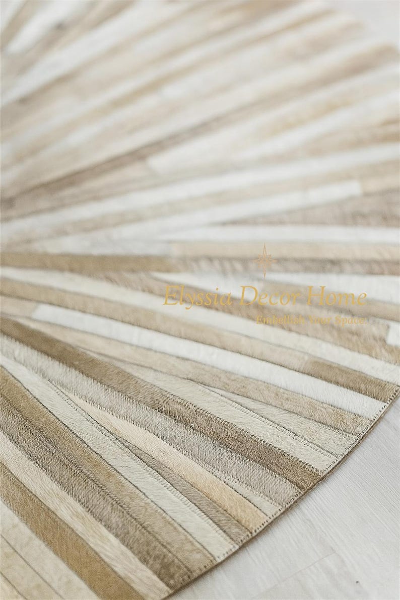 May include: A beige and white cowhide rug with a radial striped pattern. The rug features alternating stripes of light beige, tan, and white, creating a textured surface. The rug is designed for home decor.