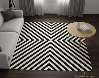 May include: A black and white geometric patterned area rug. The rug features a repeating pattern of black and white stripes that converge in the center. The rug is rectangular and covers a dark wood floor.