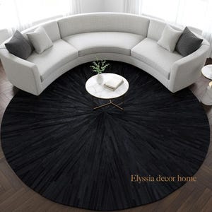 May include: A contemporary living room arrangement with a curved, pale grey sofa and grey and white cushions. A round, black rug with a radial design is under a white marble coffee table. A potted plant and a gold floor lamp complete the scene.
