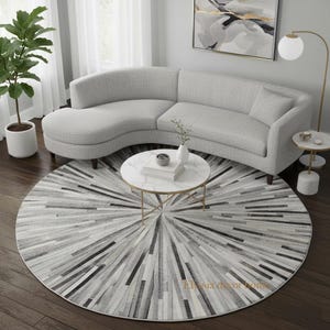 Peut inclure: Un salon moderne avec un canapé incurvé gris clair, une table basse ronde en marbre et un tapis circulaire avec un motif radial en nuances de gris et de noir. Un pot de plante et une lampe décorative complètent l'ambiance.