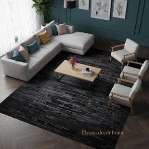 May include: An interior shot of a modern living room with a light gray sectional sofa, a wooden coffee table, and two white armchairs. A large black rug with a brick pattern covers the floor. The text "Elyssia decor home" is visible on the rug.