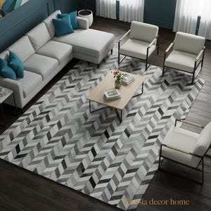 May include: A modern living room setup featuring a light gray sectional sofa with teal accent pillows, white armchairs, and a wooden coffee table. A large area rug with a gray and black chevron pattern covers the floor.