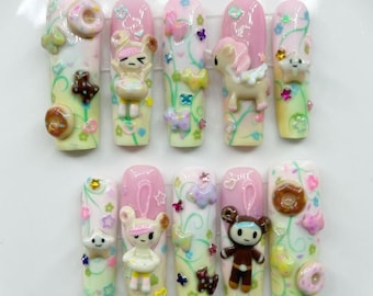 May include: A set of ten artificial nails with a light pink and cream base, adorned with 3D cartoon characters, donuts, and floral accents. The nails feature a variety of designs, including a bunny, a bear, and a unicorn, with colorful embellishments.