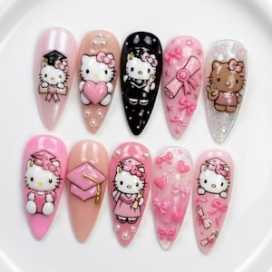 May include: A set of ten long, almond-shaped artificial nails with various designs. The nails feature Hello Kitty characters in graduation attire, bows, hearts, and diploma scrolls. Colors include pink, black, and nude.