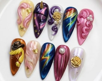 May include: A collection of ten artificial nails with various designs. The nails feature a range of colors, including pink, purple, blue, and gold, with decorative elements such as butterflies, pearls, and a golden rose. Some nails have 3D sculpted designs.