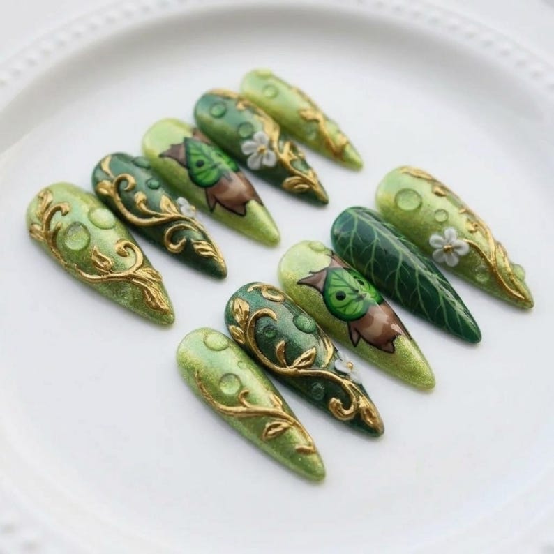 Puede incluir: Diez u&ntilde;as postizas en forma de almendra, en tonos verdes variados. Las u&ntilde;as est&aacute;n decoradas con filigranas doradas, dise&ntilde;os de hojas y peque&ntilde;as flores blancas. El dise&ntilde;o est&aacute; inspirado en la naturaleza, con un acabado elegante y detallado.