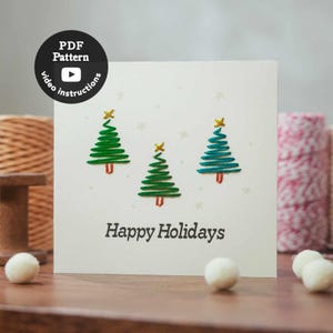 Könnte beinhalten: Eine quadratische weiße Grußkarte mit drei gestickten Weihnachtsbäumen in Grüntönen, kleinen goldenen Sternen an der Spitze und braunen Stämmen. Der Text Happy Holidays ist in Schwarz unter den Bäumen gedruckt. Enthält ein PDF-Muster-Symbol.