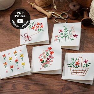 May include: Five white cards with embroidered floral designs. The cards feature various flower arrangements, including bouquets, single stems, and a basket of flowers. The text "PDF Pattern" and "video instructions" are on a black circle.