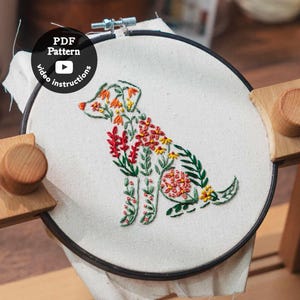 Könnte beinhalten: Stickrahmen mit einem floralen Hunde-Design. Der Hund ist mit grünem Faden umrandet und mit roten, orangefarbenen und gelben Blumen gefüllt. Der Rahmen wird in einem Holzrahmen gehalten. Der Text auf dem Bild lautet "PDF Pattern video instructions."