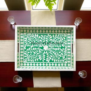 May include: A rectangular white serving tray with a green floral design and handles. The tray has a white border and the text "Home Crafted Furniture" in the center. The tray is on a dark brown table with four glasses.