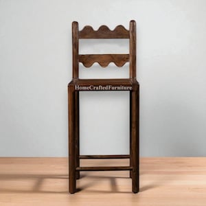 K&ouml;nnte beinhalten: Ein hoher, dunkelbrauner Holzstuhl mit einem wellenf&ouml;rmigen Oberteil und zwei horizontalen St&uuml;tzen. Der Stuhl hat einen rechteckigen Sitz und vier gerade Beine. Der Text "HomeCraftedFurniture" ist auf die Vorderseite des Stuhls gedruckt.