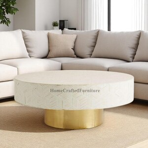 Può includere: Un tavolino rotondo con piano color crema e motivo geometrico sui lati. La base è dorata. Il testo "HomeCraftedFurniture" è stampato sul lato del tavolo.