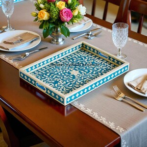 May include: A rectangular serving tray with a teal and white floral design. The tray has a white border with a teal floral pattern and blue handles. The tray is set on a table with a floral centerpiece, plates, and silverware.