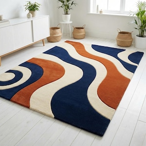 Peut inclure: Un tapis rectangulaire présentant un motif ondulé audacieux composé de sections bleu marine profond, orange brûlé et crème. Le design se compose d'épaisses courbes fluides qui parcourent toute la surface, créant un effet visuel abstrait et rythmé.
