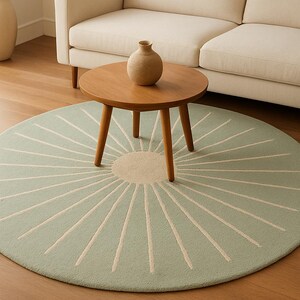May include: A round, light green rug with a sunburst design. The rug features a central beige circle with radiating cream-colored lines. A wooden coffee table with a vase sits on top of the rug. A beige sofa is in the background.