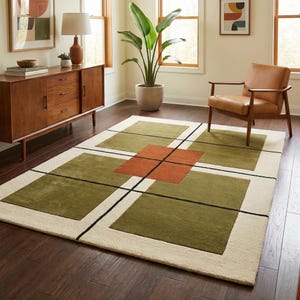 May include: A rectangular area rug featuring a geometric pattern of large olive green squares and a central burnt orange square, all separated by thin black lines on a cream-coloured background. The rug has a low-pile texture and clean edges.