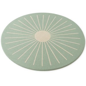 May include: A round rug with a sunburst design. The rug features a light green background with a cream-colored sun in the center and radiating lines. The rug is a soft, decorative floor covering.