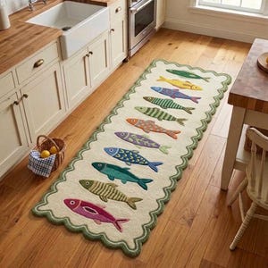 May include: A rectangular runner rug with a scalloped green border on a cream background, featuring a vertical row of ten embroidered fish in various colors including yellow, blue, green, orange, purple, and pink, arranged on a wooden floor.